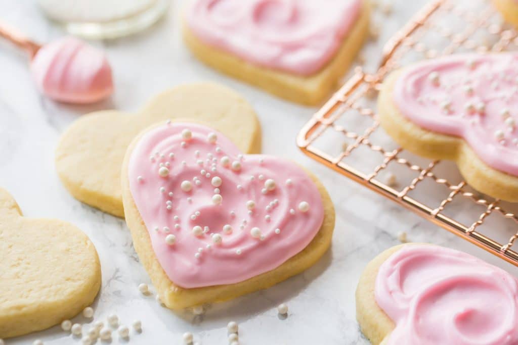 Horizontal image of heart-shaped soft sugar cookies with pink sugar cookie icing and sprinkles.