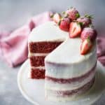 Moist triple-layer red velvet cake with cream cheese frosting and fresh strawberries.