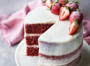Moist triple-layer red velvet cake with cream cheese frosting and fresh strawberries.
