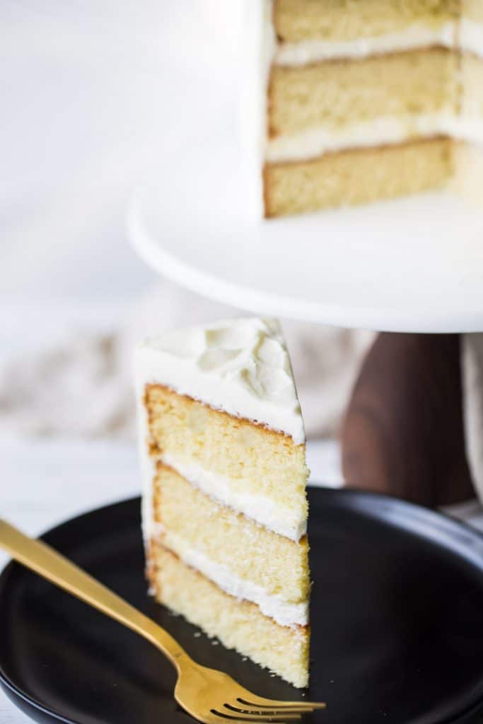 A tall slice of easy homemade vanilla cake recipe, baked, filled, and frosted.