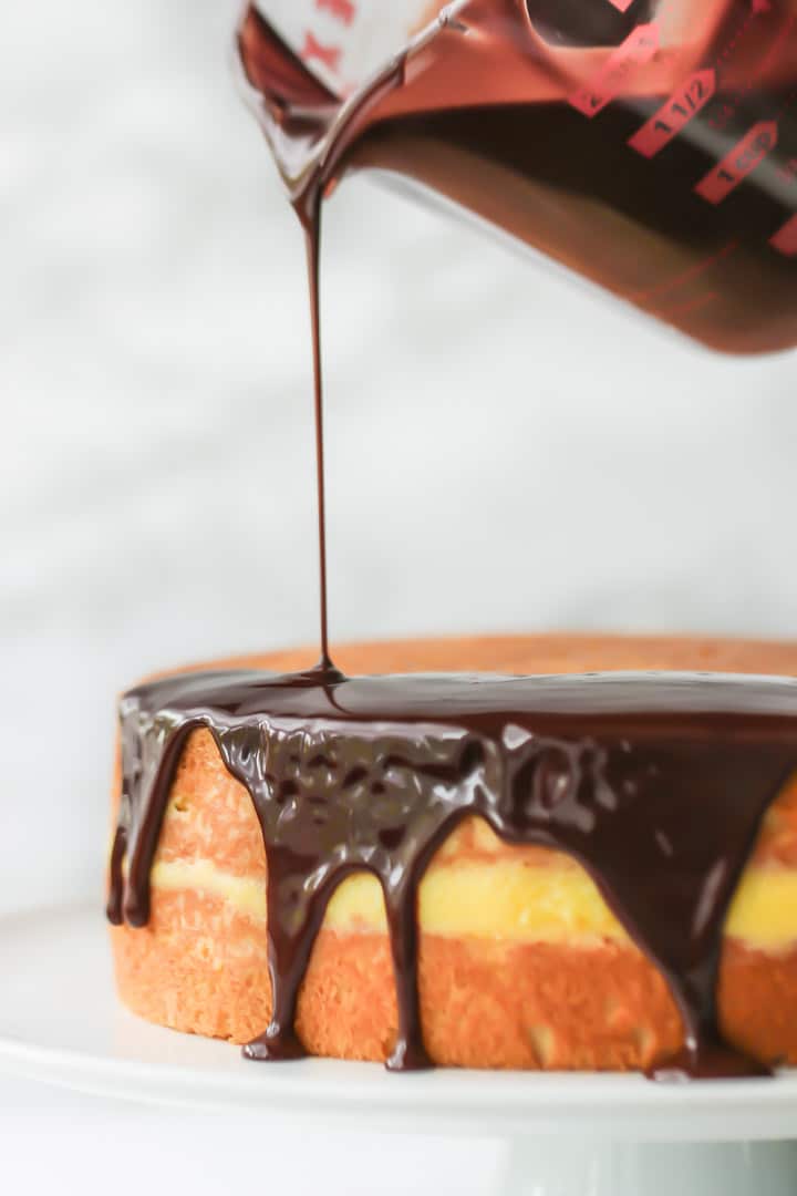 Chocolate topping being poured over vanilla sponge filled with creme patissiere to make classic Boston Cream Pie.