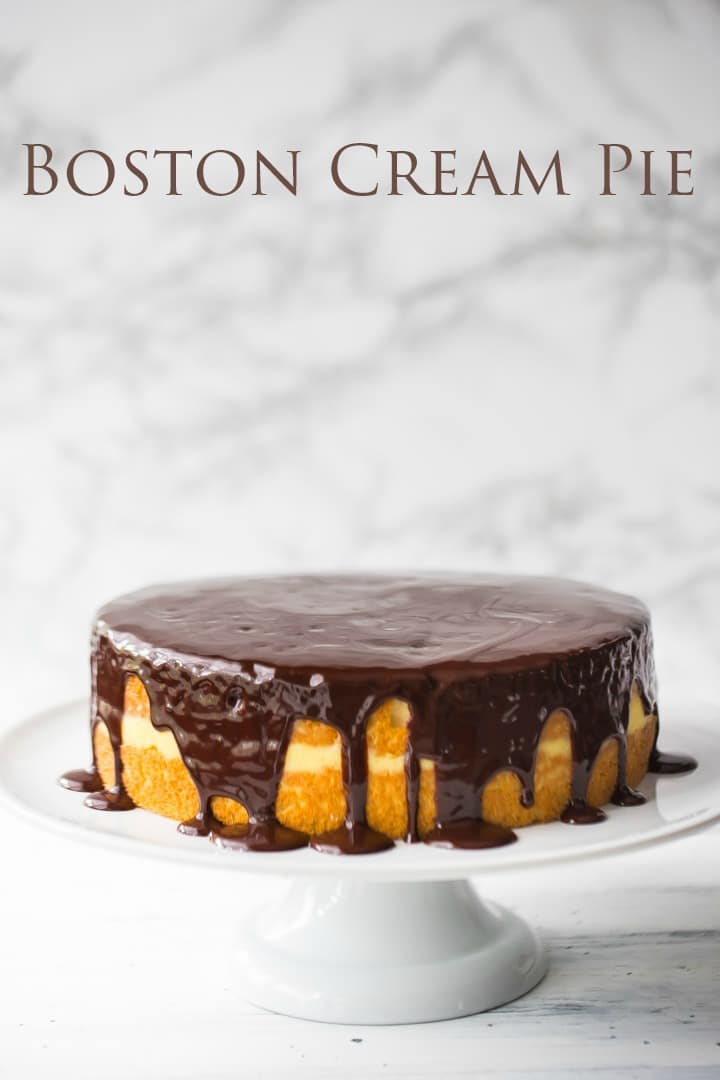 Traditional Boston Cream Pie on a cake stand with sponge cake, vanilla pudding, and dark chocolate icing.