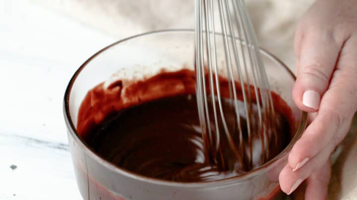 Whisking chocolate glaze in a glass bowl.