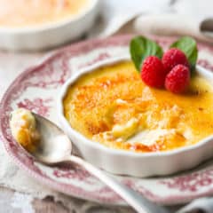 Creme brulee in a shallow dish on a vintage plate, with fresh raspberry and mint garnish.