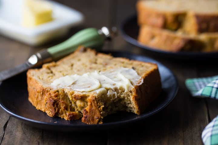 Horizontal image of a slice of zucchini bread, buttered and served on a plate with a plaid napkin.