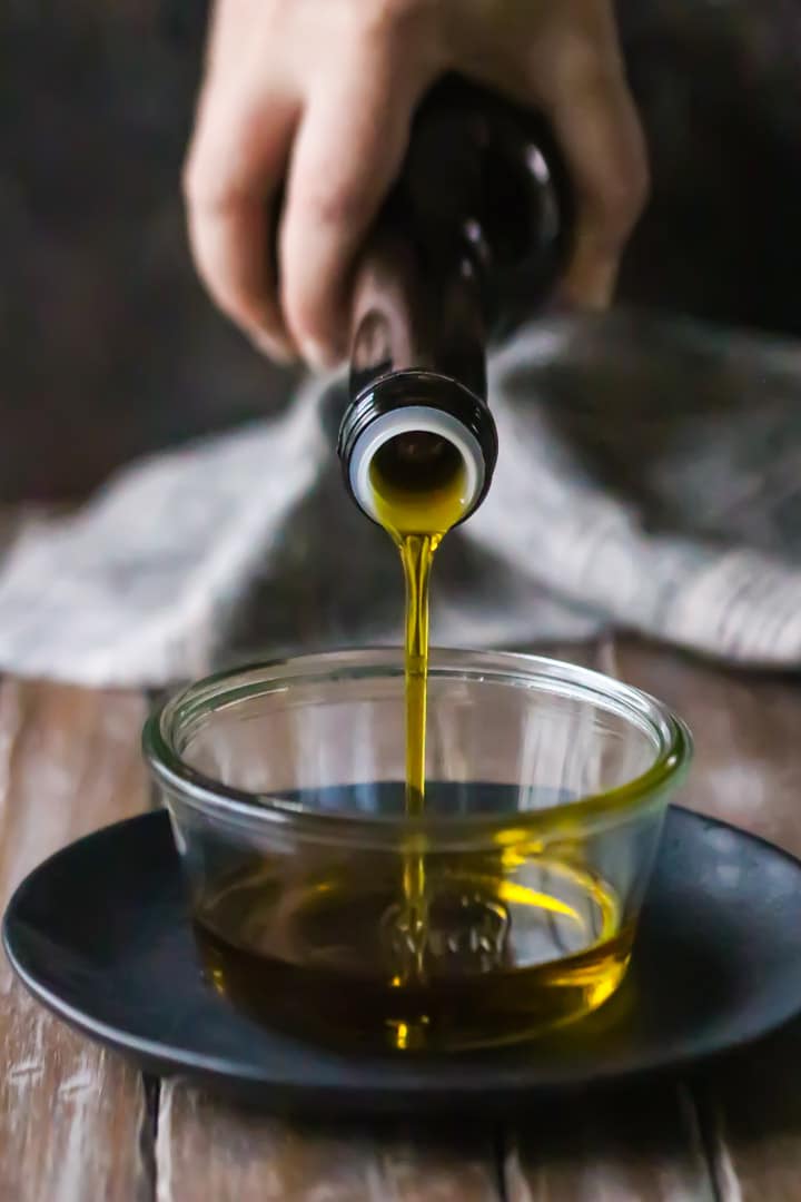 Pouring olive oil from a bottle into a glass dish, to make a Spanish olive oil cake recipe.
