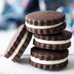 Homemade Oreos stacked on a white surface with a blue napkin in the background.