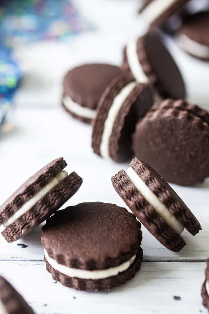 Homemade Oreo cookies tumbling over a distressed white tabletop.