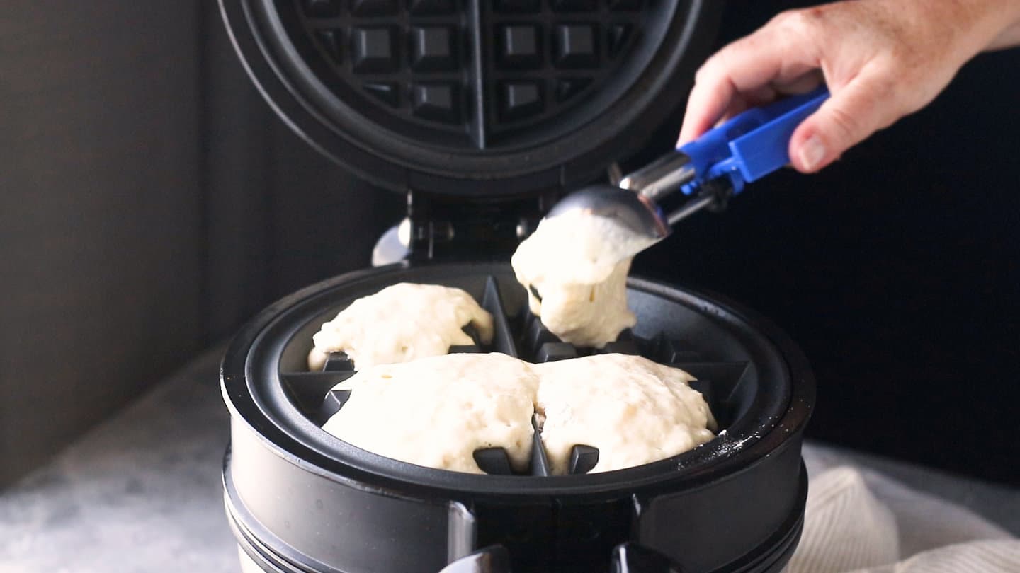 Scooping batter onto a preheated waffle maker.