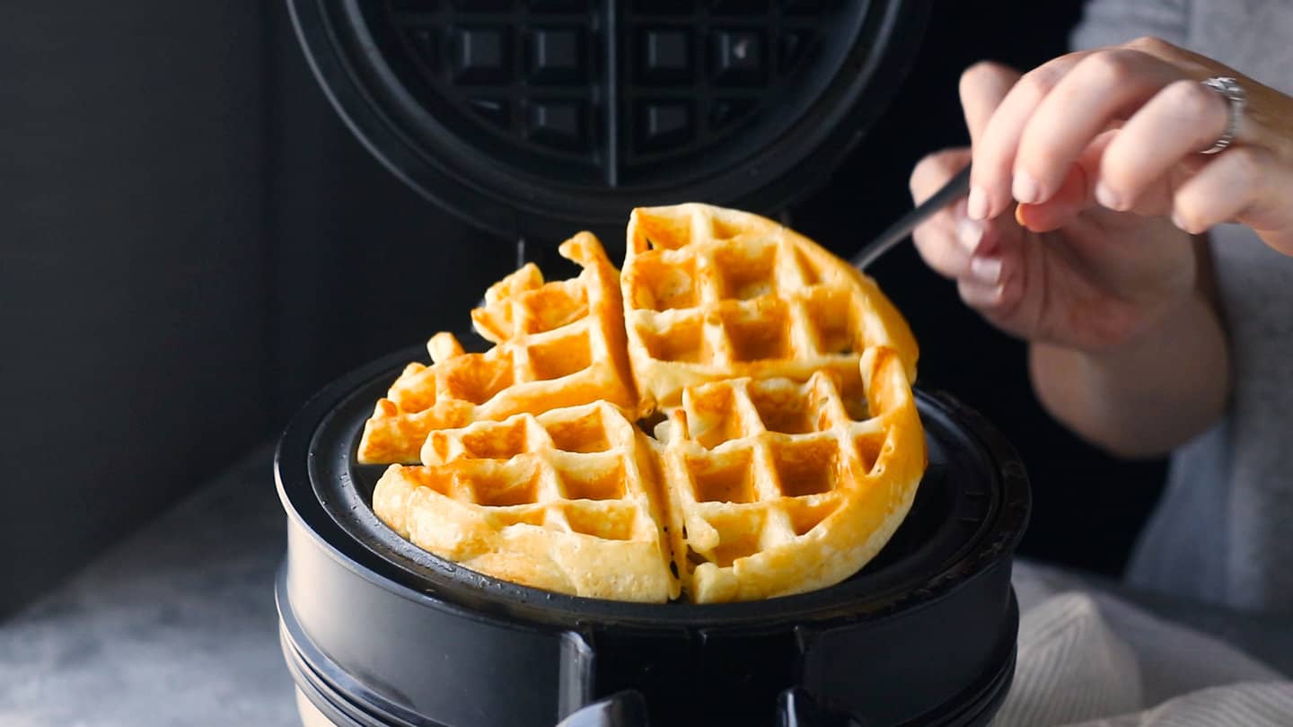 Lifting a cooked waffle out of the waffle maker.