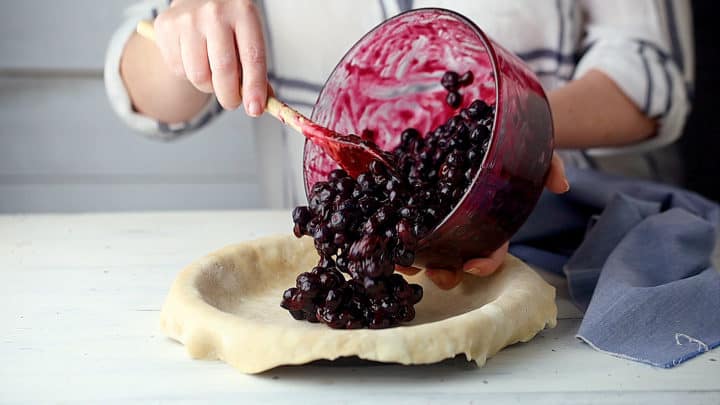 Transferring blueberry pie filling to an unbaked pie shell.