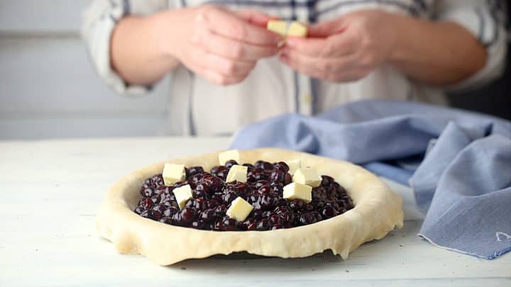 Dotting blueberry pie with butter.