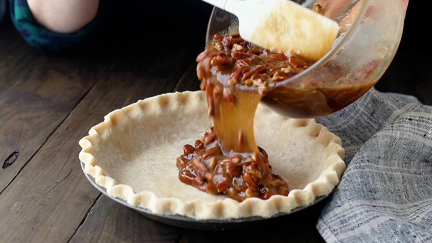 Pouring pecan pie filling into crust.