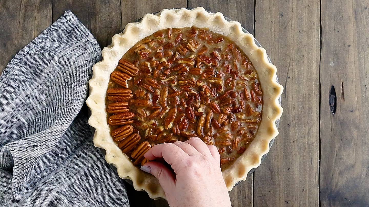 Garnishing the outside edge of a pecan pie with pecan halves.