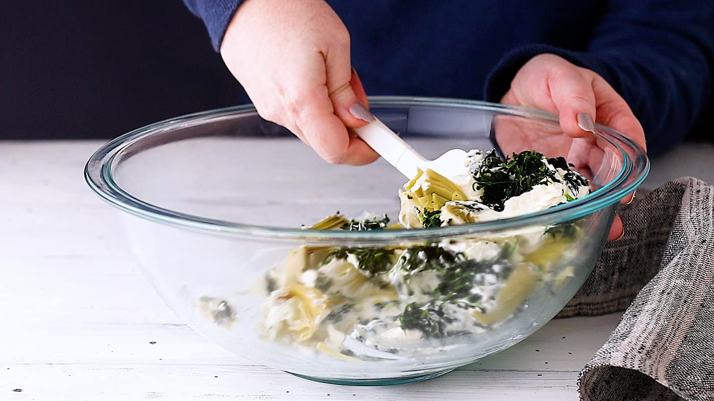 Folding spinach and artichoke hearts into softened cream cheese.