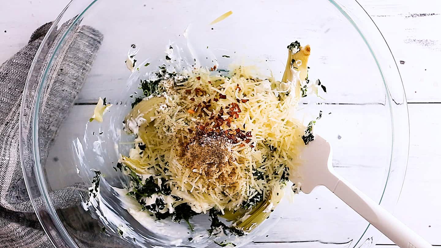Adding parmesan and seasonings to spinach artichoke dip.