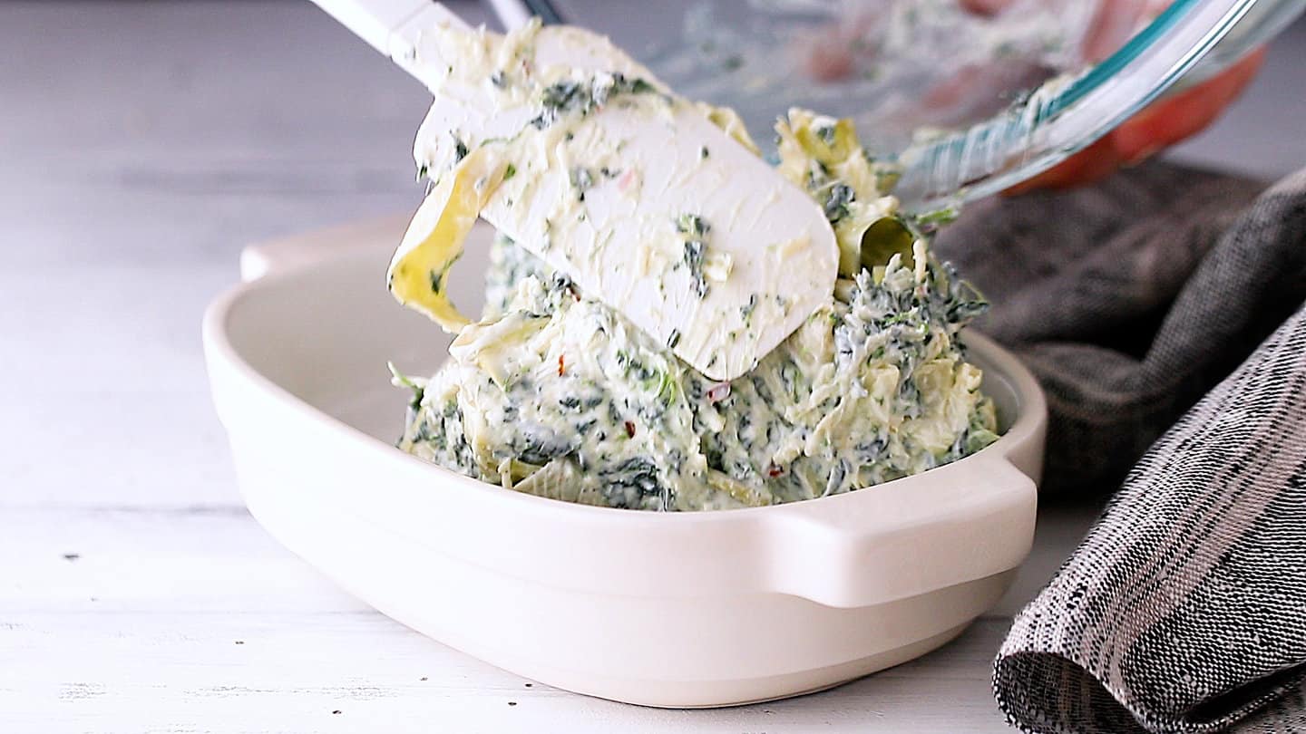 Transferring spinach artichoke dip to an oven-safe baking dish.
