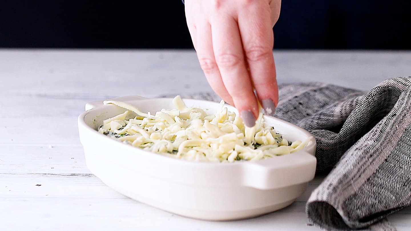 Topping spinach artichoke dip with shredded mozzarella.