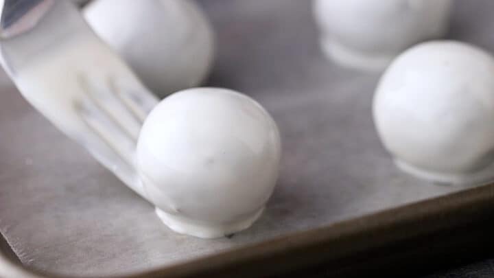 Placing coated Oreo balls on a parchment-lined baking sheet with a fork.