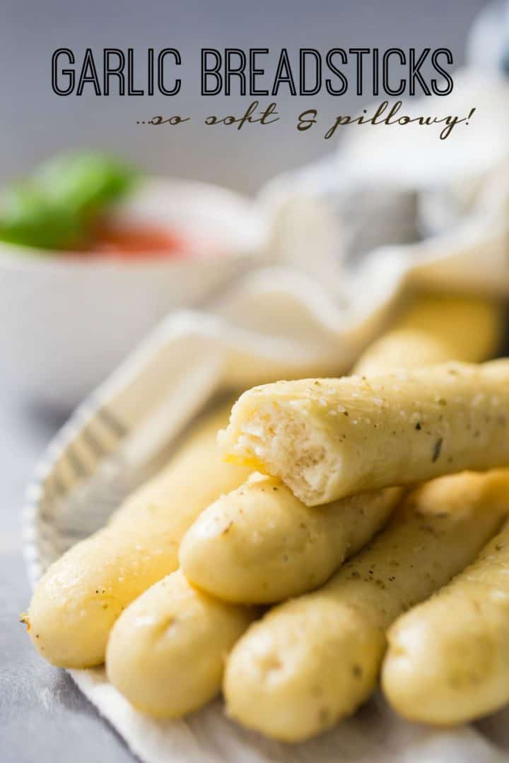 Image of soft garlic breadsticks with marinara sauce in the background and a text overlay. 