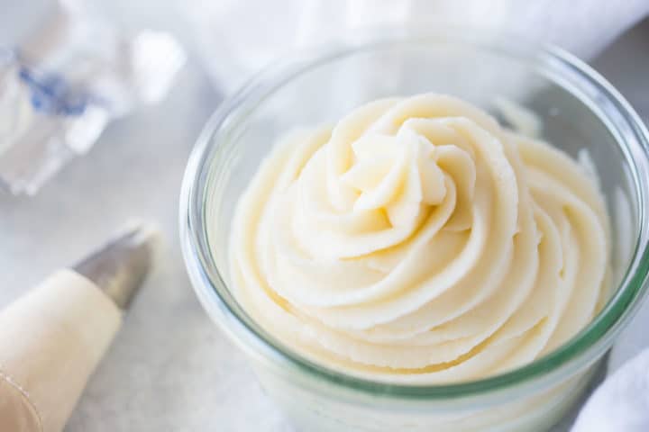 Close up of a glass bowl filled with cream cheese frosting, piped in a swirl pattern.