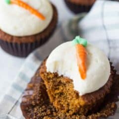 A carrot cake cupcake with a bite taken out of it, exposing the moist, sweet, cake under the cream cheese frosting