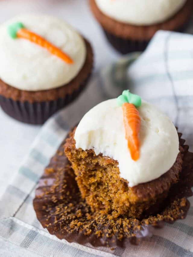 A carrot cake cupcake with a bite taken out of it, exposing the moist, sweet, cake under the cream cheese frosting