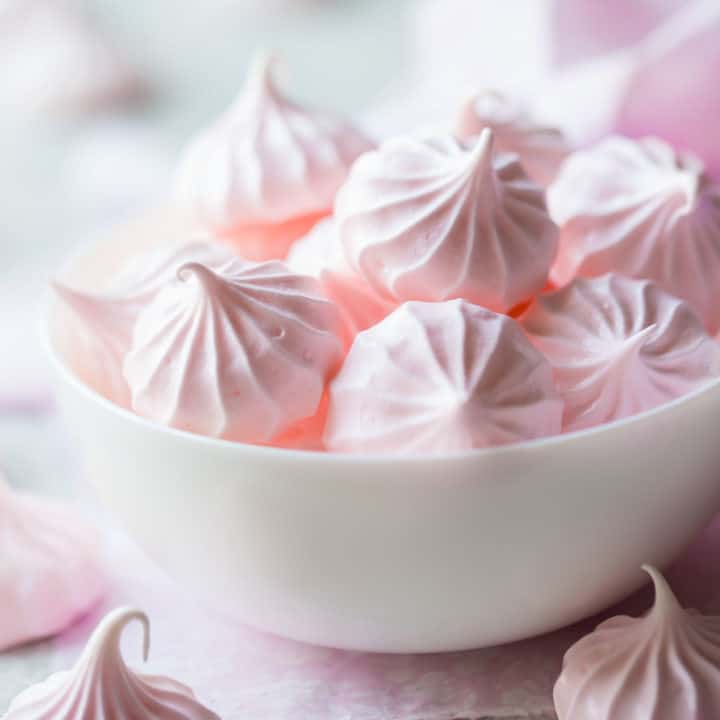 Pale pink meringue kisses in a white bowl.