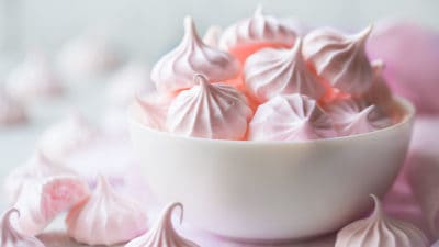 Baby pink baked meringue kisses in a white bowl.