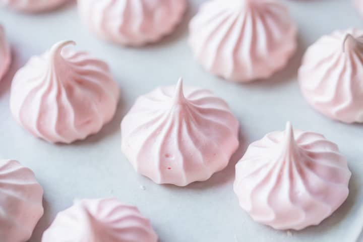 Light pink baked meringue kisses on a parchment-lined baking sheet.