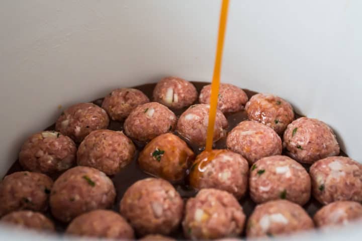 Pouring sweet and sour sauce over meatballs in a slow cooker.