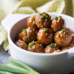Glazed sweet & sour meatballs in a white crock with scallions.