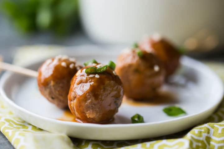 Sweet and sour meatballs on toothpicks with scallions and sesame seeds.
