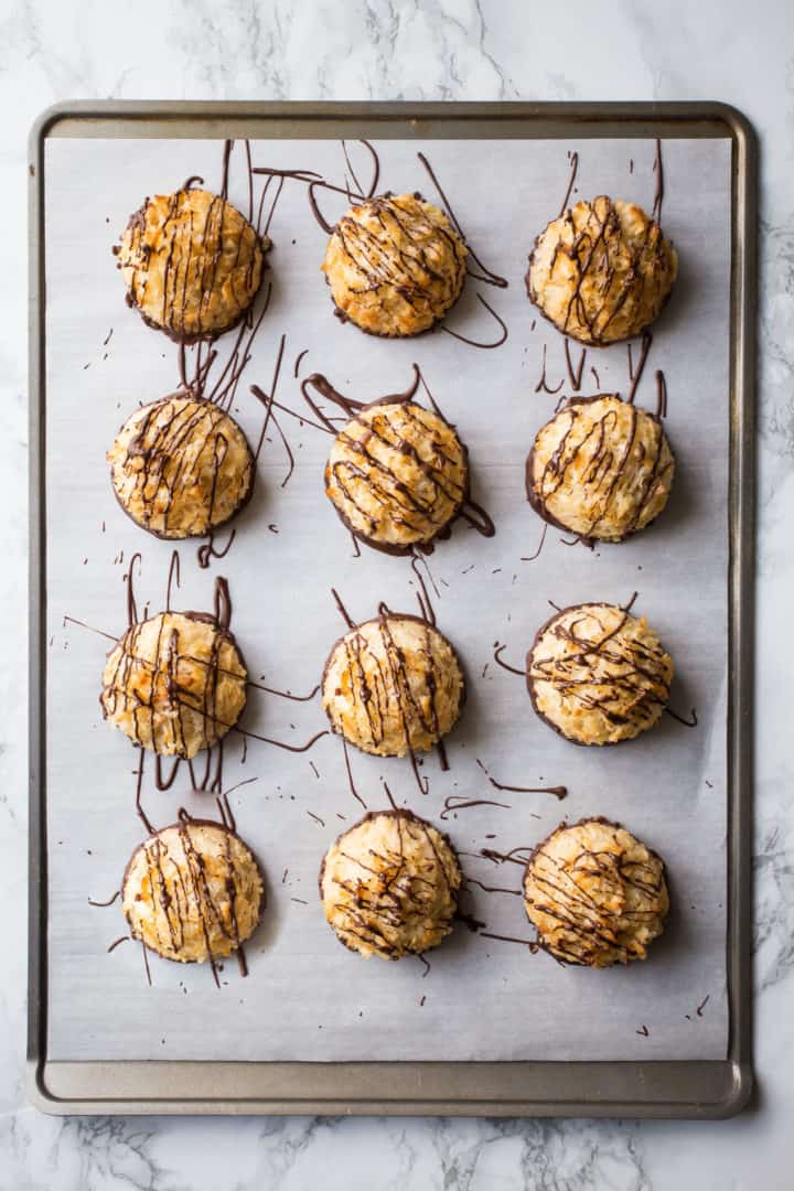 Overhead image of coconut macaroons dipped in dark chocolate on a parchment-lined baking sheet.