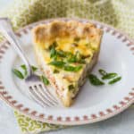A slice of quiche Lorraine on a china plate with a green printed napkin.