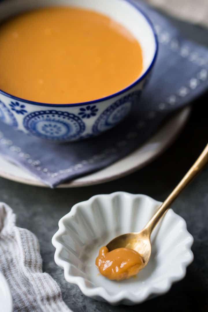 A spoonful of dulce de leche in a small white dish, with a larger bowl of dulce de leche in the background.