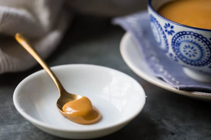 Gold spoonful of dulce de leche caramel on a white dish with a blue patterned bowl in the background.