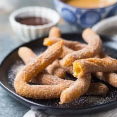 Homemade churros on a dark plate with chocolate sauce and dulce de leche in the background.