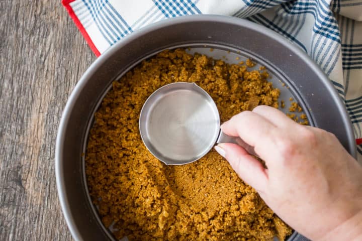 Pressing graham cracker crust into an even layer with the bottom of a measuring cup.