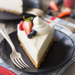 A perfect slice of no-bake cheesecake with whipped cream and berries, on a dark blue plate with a vintage silver fork.