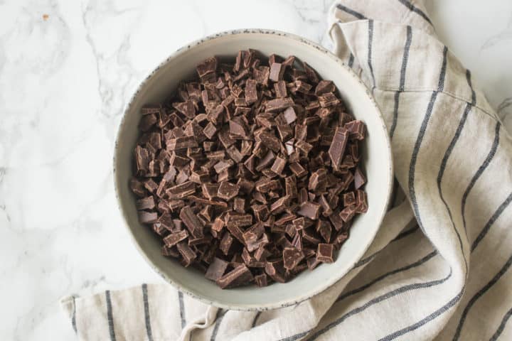 Chopped chocolate in a bowl with a striped kitchen towel.