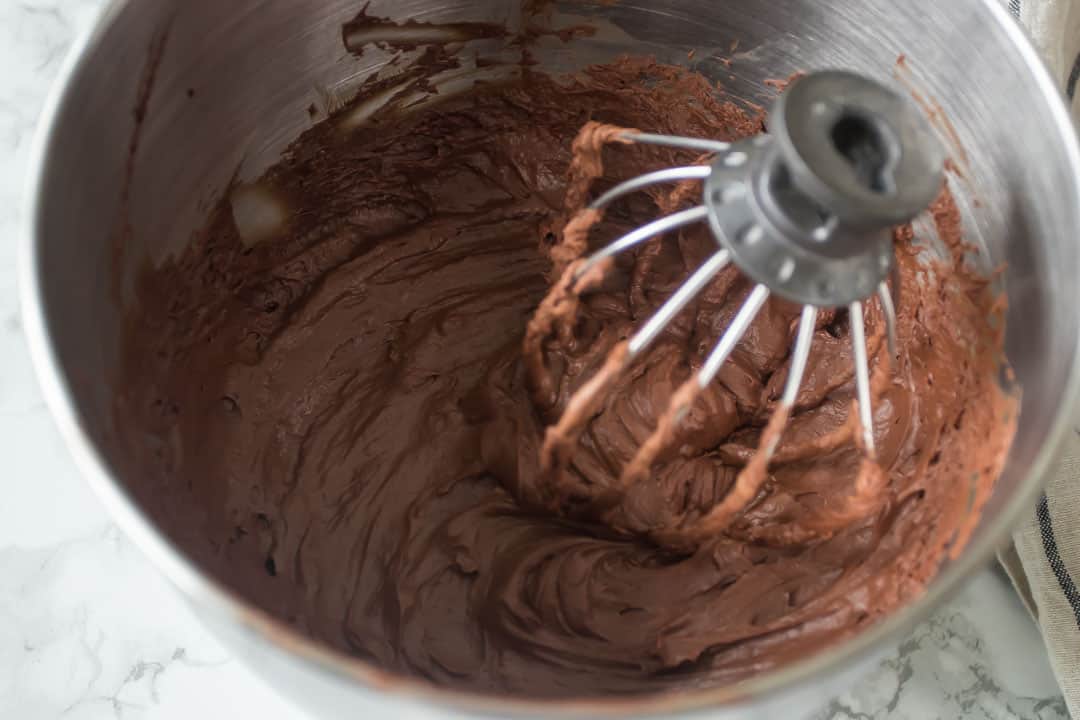 Whipped ganache in a metal mixing bowl with a whisk attachment from a mixer.