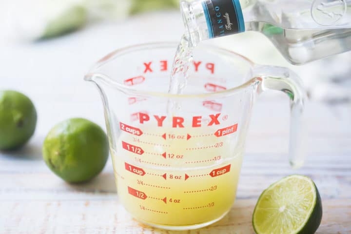 Pouring tequila into liquid measuring cup with freshly squeezed lime juice.
