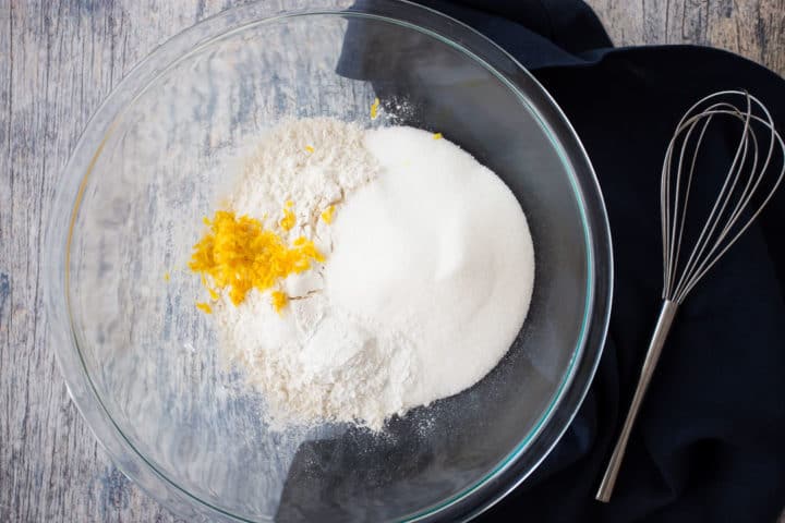 Dry ingredients in a large glass bowl, with a dark blue linen napkin and a whisk.