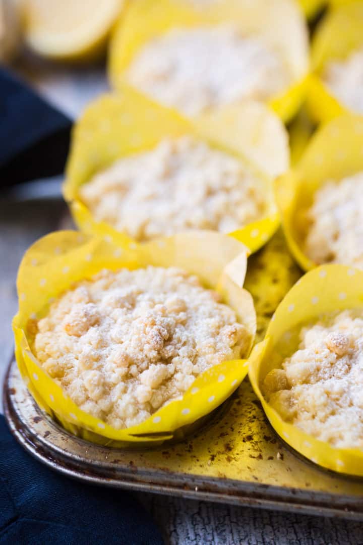 Lemon crumb muffins in a pan with yellow liners and powdered sugar on top.