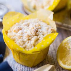 Lemon crumb muffin in a yellow tulip cup with fresh lemon in the background.