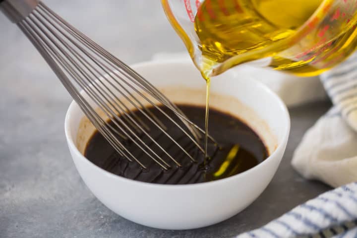 Drizzling and whisking oil into vinegar.