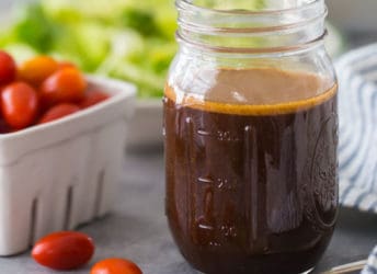 Mason jar of homemade balsamic vinaigrette dressing, with tomatoes and lettuce in the background.