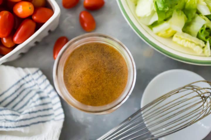 Overhead view of balsamic vinaigrette dressing, with a whisk, tomatoes, and lettuce.
