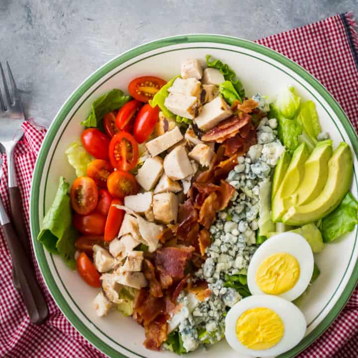 Overhead image of cobb salad in a bowl, with a red checked napkin.